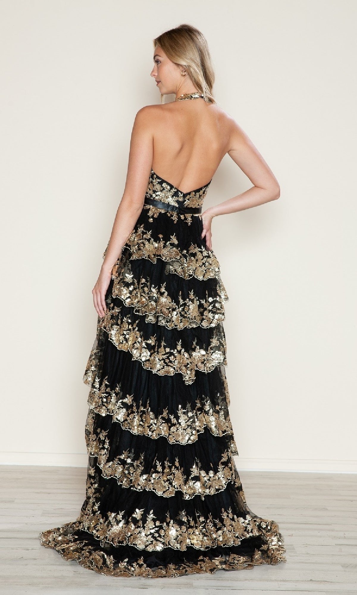A woman faces away against a plain background, wearing the Long Prom Dress: Poly USA 9618—a strapless black sequin gown with gold floral embroidery and tiered ruffles.